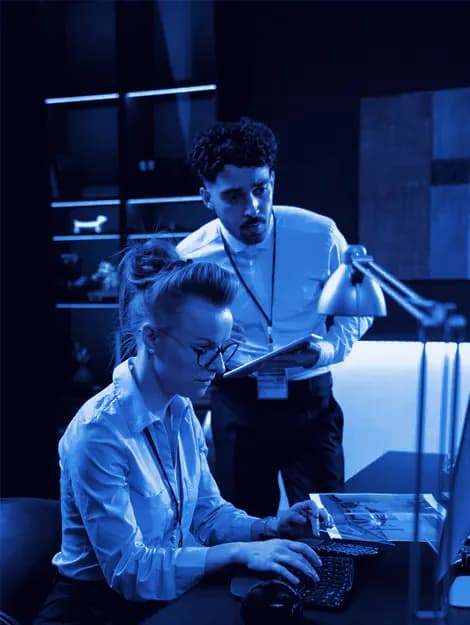 Engineer with a tablet helping an employee at her workstation